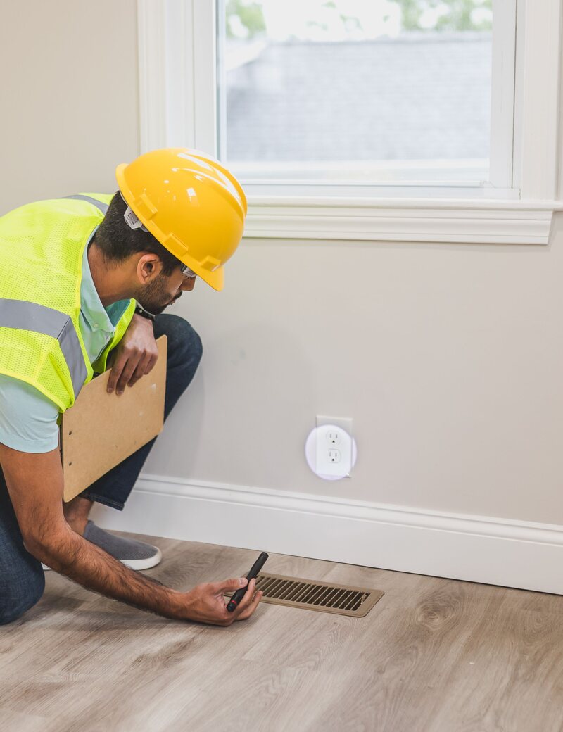 Technician inspecting a floor air vent in a home